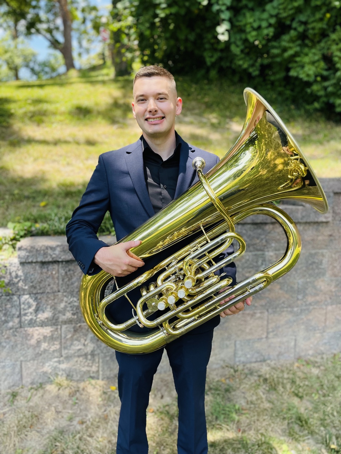 Studio portrait of Max Crofton in a navy suit, holding his tuba.