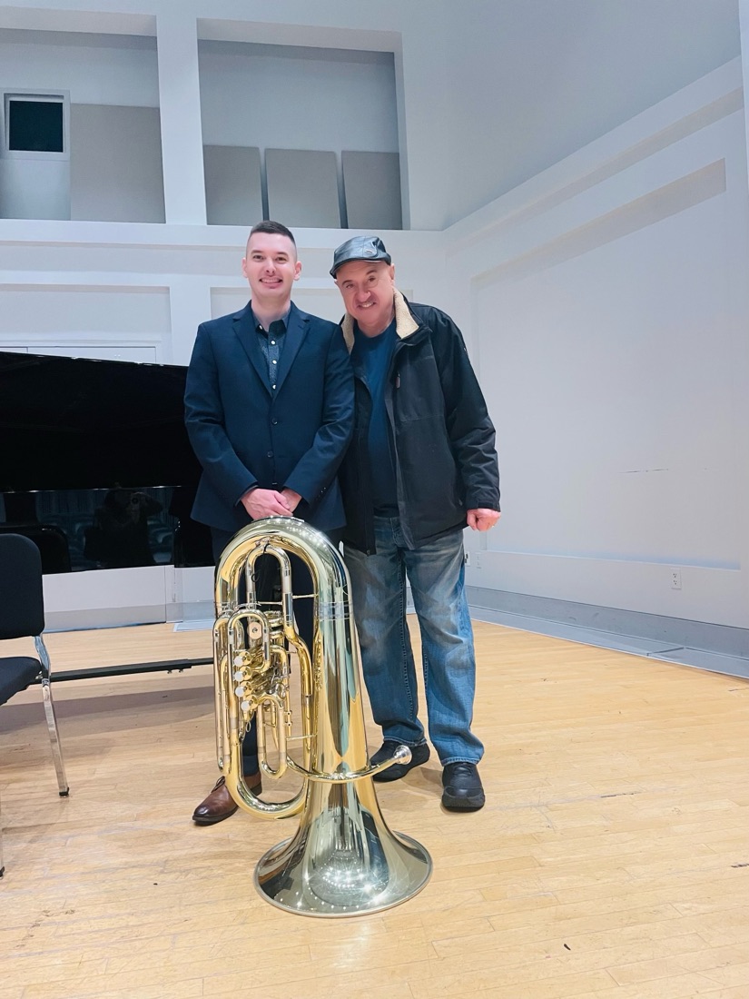 Max Crofton standing with his tuba beside his mentor on a recital hall stage.