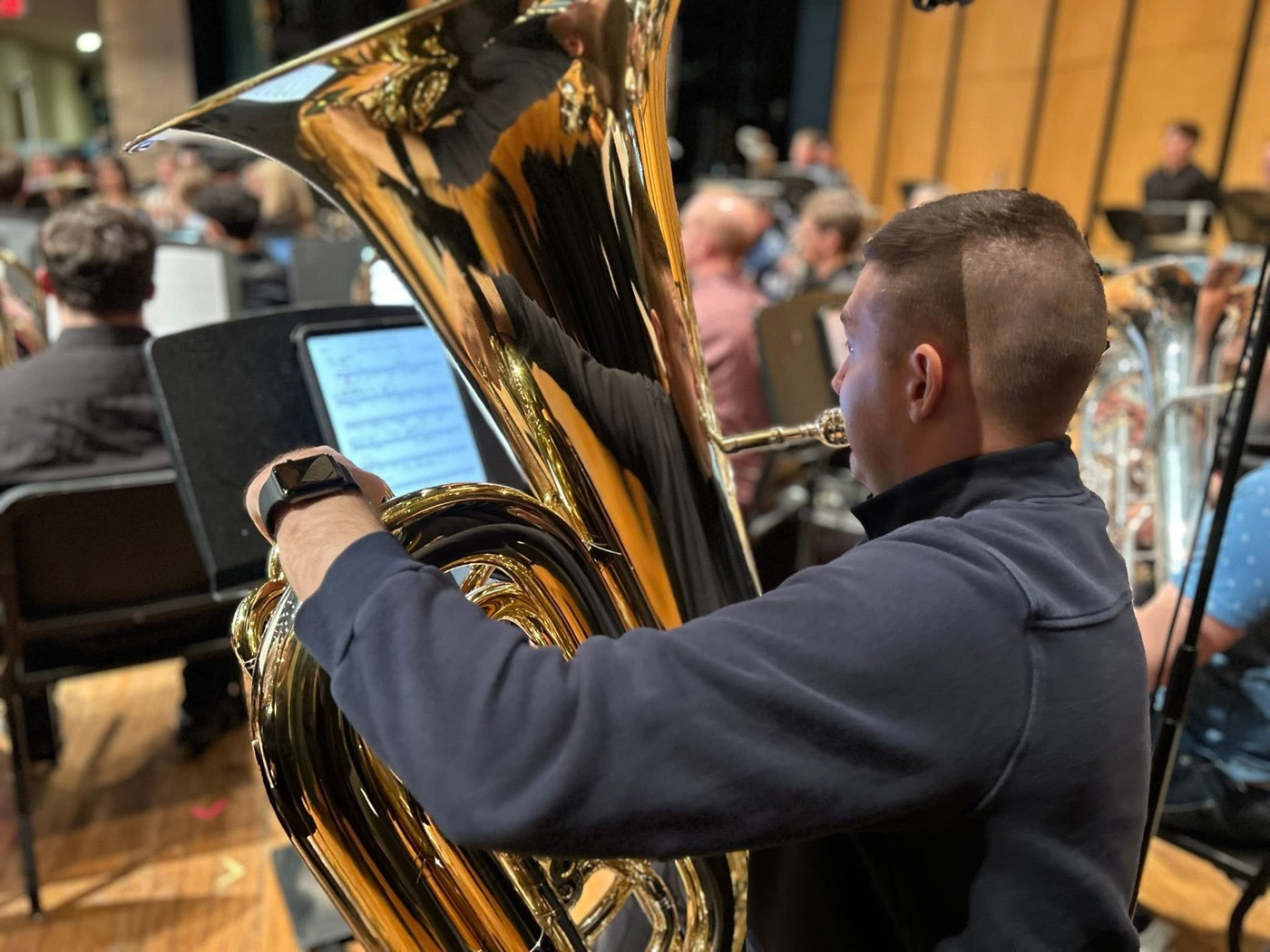 Max Crofton performing on tuba with a concert band on stage.